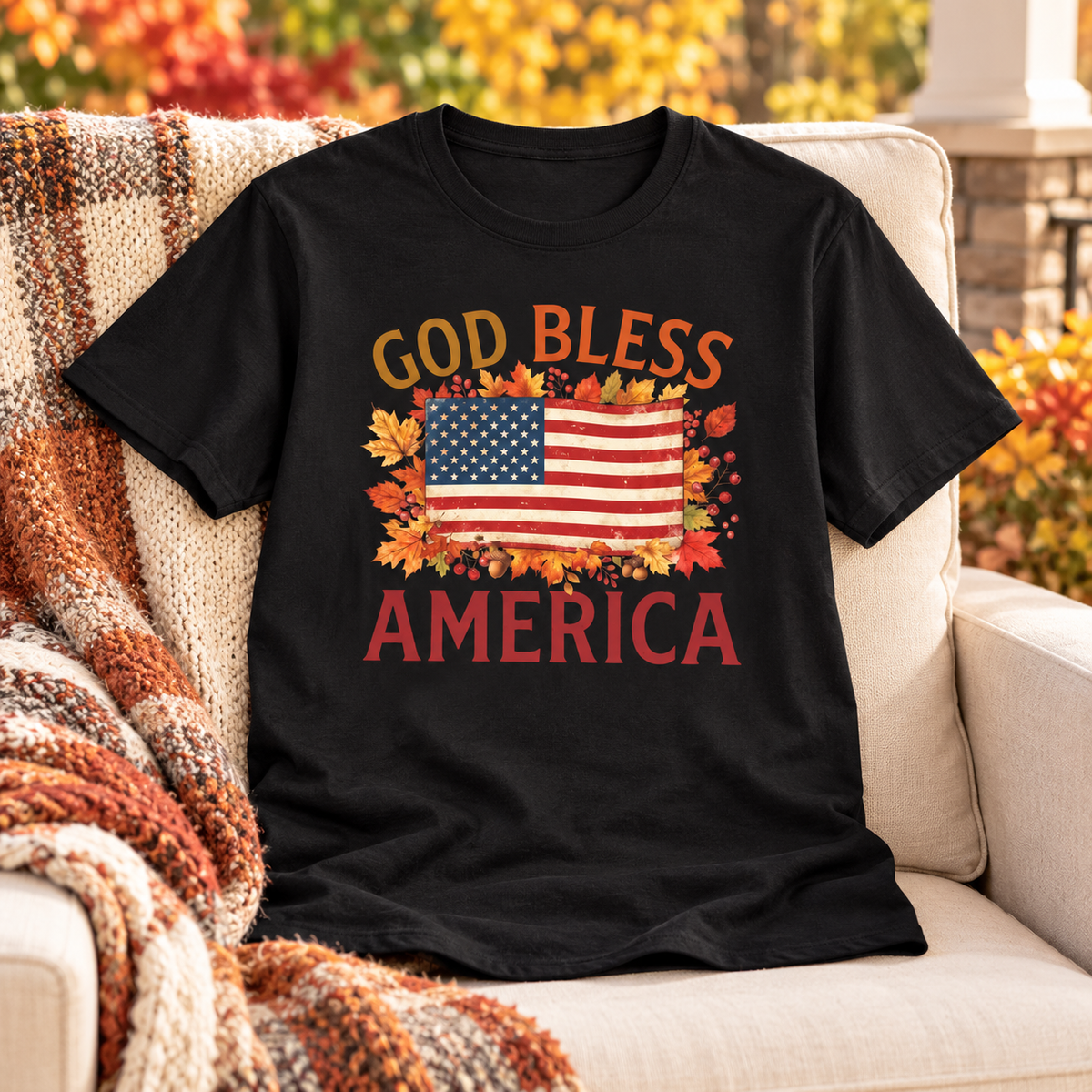 Black God Bless America Shirt — no person, shirt neatly arranged front fully visible on a cream upholstered porch armchair, gentle fall foliage behind